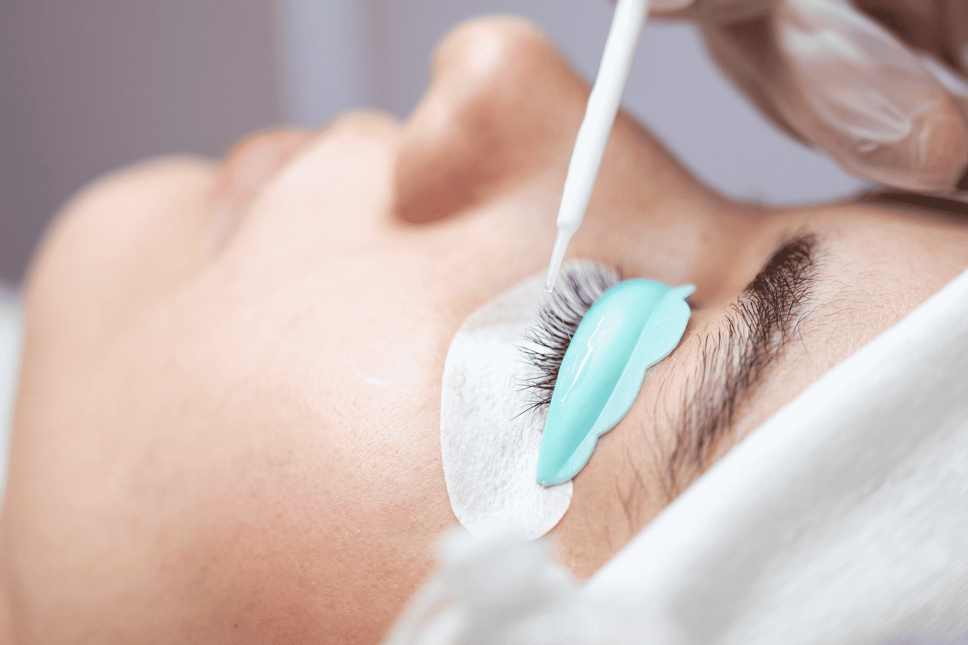 Beautician applying lash lift treatment to a client's eyelashes with a brush.