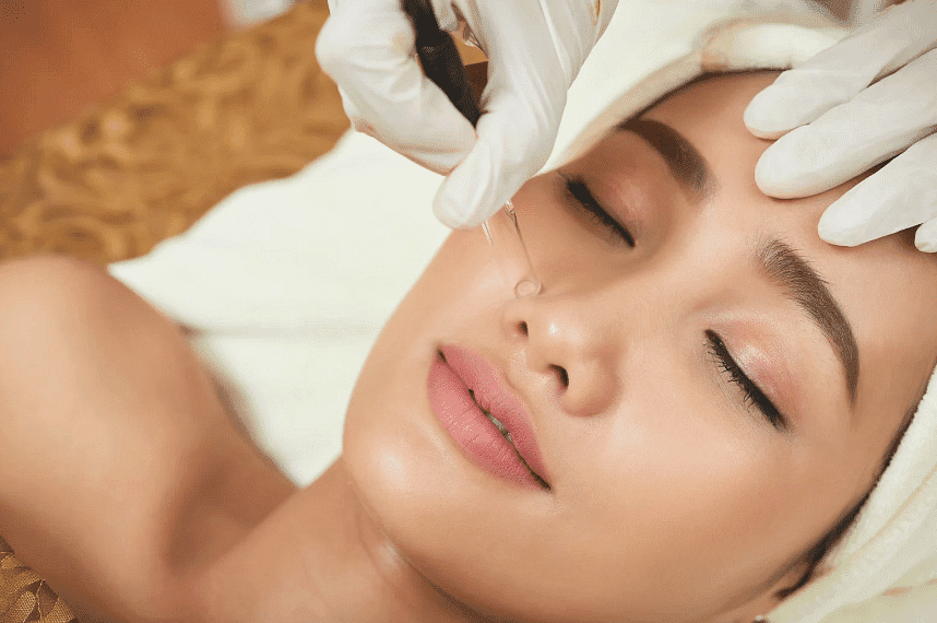 A person receiving a facial treatment with cosmetologist's hands applying a needle to the skin.
